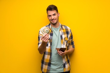 Handsome man over yellow wall holding a wallet