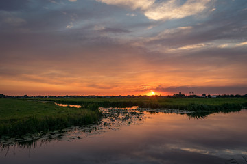 Wall Mural - the sun sets on the horizon of the dutch countryside. a beautiful colored sky is reflected in the wa