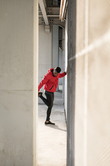  Black athlete stretching quadriceps during running urban workout.