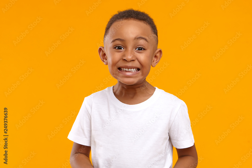 Human emotions, feelings and reaction. Positive emotional dark skinned little boy of 10 year old making funny facial expression, smiling broadly, showing white perfect teeth, posing isolated - obrazy, fototapety, plakaty 
