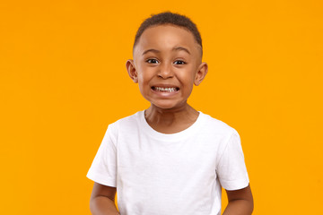 Wall Mural - Human emotions, feelings and reaction. Positive emotional dark skinned little boy of 10 year old making funny facial expression, smiling broadly, showing white perfect teeth, posing isolated