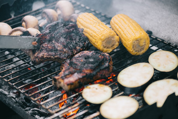 Poster - selective focus of tweezers and juicy delicious steaks grilling on bbq grid with mushrooms, corn and sliced eggplant
