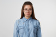 Portrait of a young pretty girl in glasses with long hair looks sad upset unhappy pouting lips, dressed in a denim shirt isolated on white background