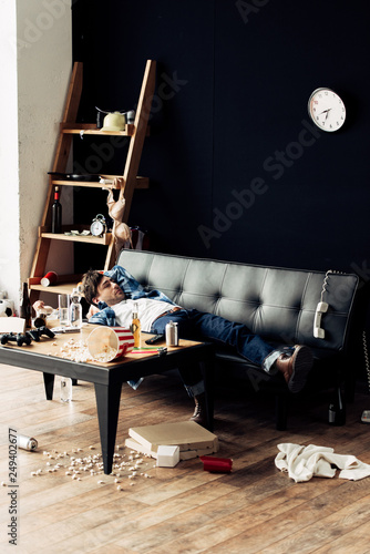 Tired Man Lying On Sofa After Party In Messy Living Room