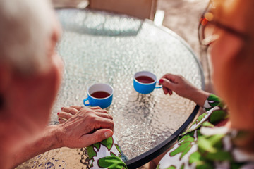 Wall Mural - Senior couple drinking tea in hotel cafe holding hands. People enjoying vacation. Close-up