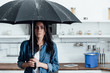 Amazed woman standing under umbrella during leak in kitchen