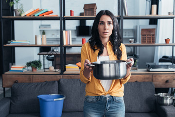 Young woman in yellow shirt holding pot in living room