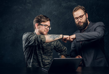 Friendship, brofist, cooperation. Two programmer's colleagues fist bumping after completion of the general project in the office against a dark wall 