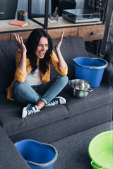 Wall Mural - Screaming woman in yellow shirt sitting on sofa under leaking ceiling