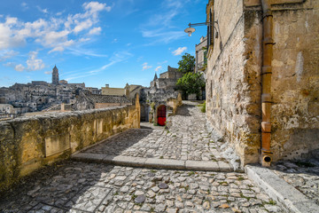 Typical forked hillside path with a red door near the Convent of Saint Agostino in the ancient city of Matera, Italy, with the church tower visible in the distance.