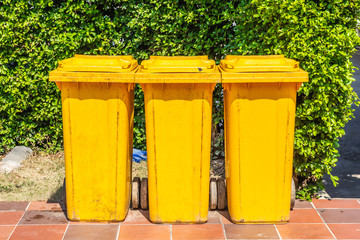 Row of yellow plastic trash bin for wate separation and recycling on green leaf background