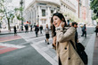 © PR Image Factory - female asian tourist with curious face smiling standing on sidewalk. people walking on zebra cross in background. young woman finding direction city tour in san francisco in america spring holidays