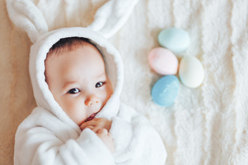 small child smiling baby in a white bunny rabbit costume easter playing with colorful easter eggs