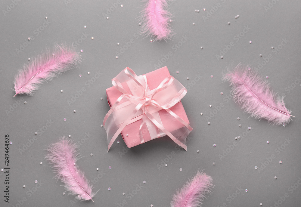 Beautiful gift and feathers on grey background