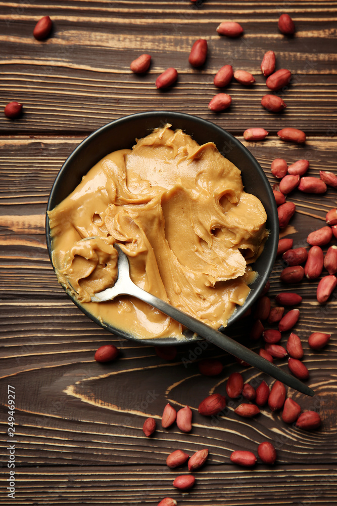 Bowl with tasty peanut butter on wooden background