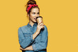 Portrait of charming young female sipping hot coffee on yellow background. Beautiful brunette lady in stylish clothes looking away. Copy space in right side. Lifestyle concept