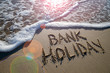 Bank Holiday message handwritten on the smooth sand of an empty beach with an oncoming wave