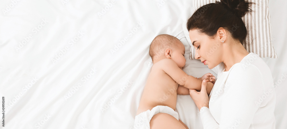 Young mom and her cute baby sleeping in bed - obrazy, fototapety, plakaty 