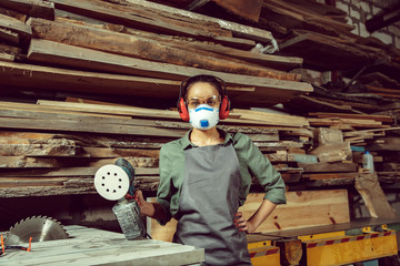 Wall Mural - Busy and serious craftswoman grinding timbers with special machine. Beautiful woman wearing safety glasses. Concept of joiner's shop and woodworking. Gender equality. Male profession