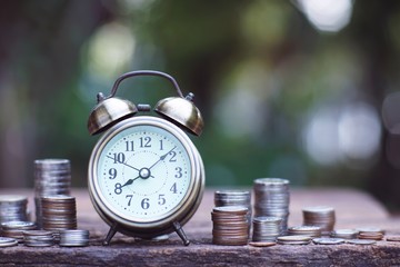 Vintage alarm clock and coin stacks on wooden table with blur green garden background, bright morning color tone, finance and business concept