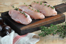 Raw Chicken Breast On A Wooden Board. The Fillet Is Decorated With Thyme Sprigs. The Composition Is Complemented With A Cloth And Green Thyme. Light Wooden Background. Close-up. Macro Shooting.