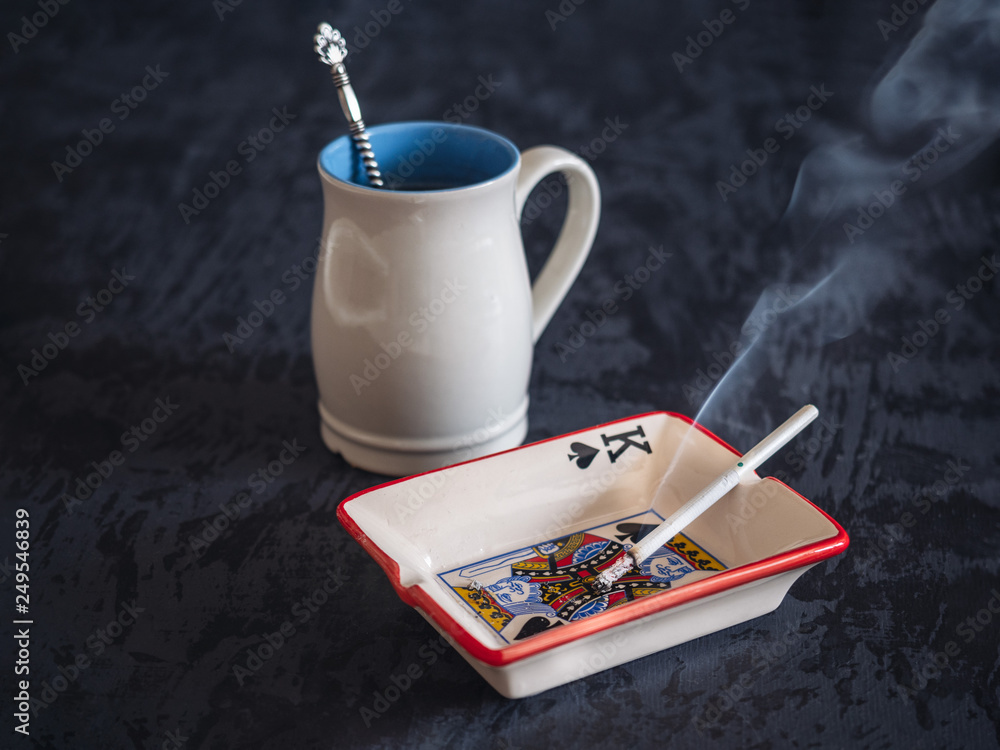tea with cigarette A high light blue cup with hot tea, a lit cigarette in an ashtray, a bad  smoking habit. Stock Photo