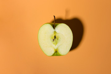 Sliced green delicious apple isolated on orange background with contrast shadows