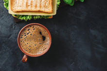 Cup With Hot Coffee And Sandwich With Grilled Toast, Salami Sausage, Salad Lettuce, Spinach Leaves And Cheese On A Dark Background, Top View