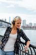 © Westend61 - USA, New York City, Brooklyn, smiling young woman standing at the waterfront with headphones and cell phone