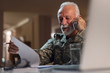 © Drazen - Smiling senior sergeant reading documents and talking on mobile phone.