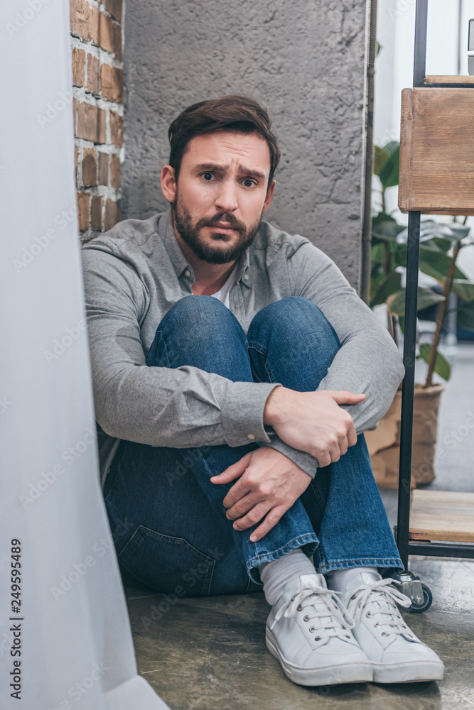 sad man sitting in corner and hugging knees on textured background in ...