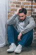 © LIGHTFIELD STUDIOS - upset man in grey shirt and blue pants sitting on floor on brown textured background in room, grieving disorder concept