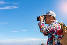 Young Man With Backpack And Holding A Binoculars Looking On Top Of Mountain
