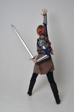 Full Length Portrait Of A  Red Haired Girl Wearing Medieval Warrior Costume And Steel Armour, Standing Pose Facing Away From The Camera On Grey Studio Background.