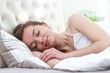 © Goffkein - Young beautiful caucasian woman covered with a blanket sleeping and relaxing on the pillow in bed in early morning. Girl resting with closed eyes in bedroom at home