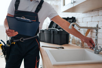 Cut view of handyman holding tool box and wrench in hands. He stand in kitchen at sink. He open water tap.