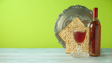 Jewish holiday Passover celebration concept with wine, matzo, and seder plate on wooden table over green background