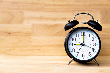 Black alarm clock on the floor and wooden background - Times concept.