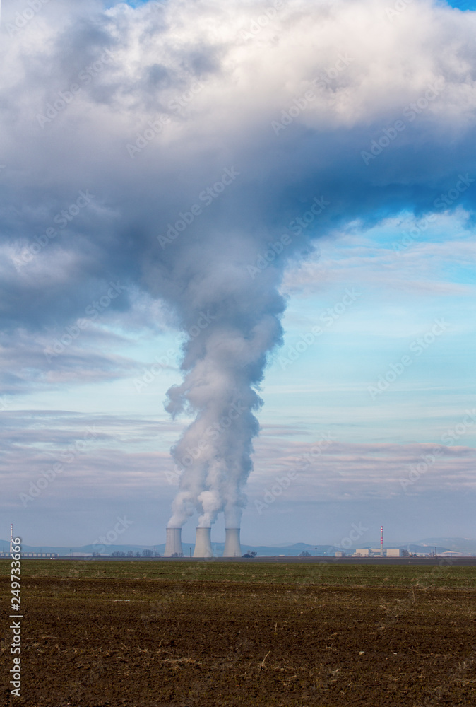 Photo Stock Cooling towers of nuclear power plant (NPP) Jaslovske Bohunice  (EBO) in Slovakia. Clouds of thick smoke from chimneys on blue sky at  winter day. Cooling towers of power plant with