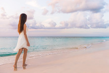 Peaceful Vacation Paradise Woman Walking On Sunset Beach With Pastel Colors Sky And Ocean For Tranquility And Serenity . Girl In White Dress Relaxing On Luxury Tropical Summer Getaway.