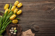 Easter background with colorful eggs and yellow tulips on wooden table. Top view with copy space