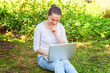 © Юлия Завалишина - Freelance business concept. Young woman sitting on green grass lawn in city park working on laptop pc computer. Lifestyle authentic candid student girl studying outdoors. Mobile Office