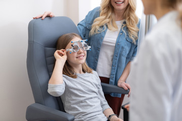 Wall Mural - Smiling little girl wearing optical trial frame in ophthalmologist cabinet