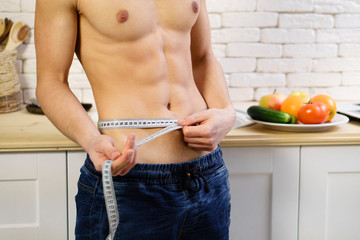 fitness, healthy lifestyle, proper nutrition, well being. athletic sporty well-formed fit man measuring his waist with tape measure