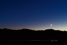 Moon, Venus, And Saturn In A Deep Blue Twilight Sky Above A Mountain Silhouette