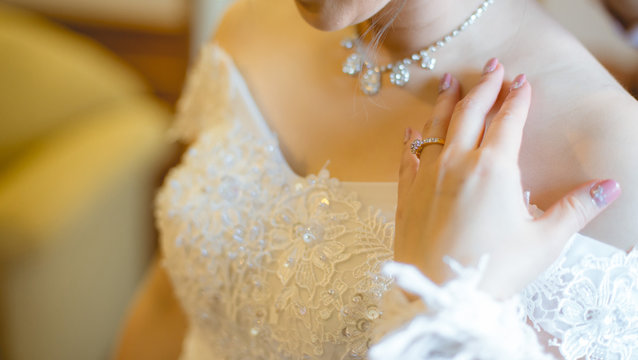 The bride in a white dress and her hand with a wedding ring wearing on her finger.