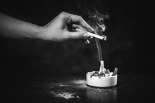 Black White Photo. A Woman's Hand Shakes Off The Ashes Of A Burning Cigarette In An Ashtray, Where There Are A Lot Of Cigarette Butts. Smoking Is Dangerous For Women's Health. Cigarette Smoke.
