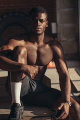 Handsome African American bodybuilder man, with naked muscular torso posing against red brick wall.