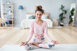 © BestForYou - Portrait of positive female yoga instructor in lotus pose on yoga mat home interior.