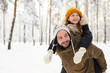 © Seventyfour - Portrait of happy little girl riding on fathers back in winter forest having fun, copy space